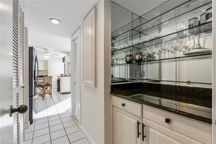 Bar featuring ceiling fan, light tile patterned flooring, dark stone countertops, and stainless steel refrigerator