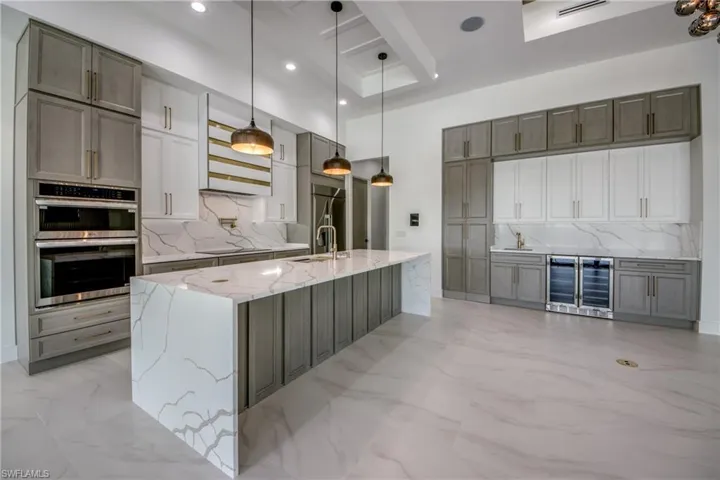 Kitchen featuring light stone counters, decorative backsplash, pendant lighting, beverage cooler, and double oven