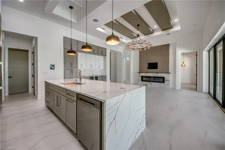 Kitchen featuring a large island with sink, a raised ceiling, light stone counters, stainless steel dishwasher, and a premium fireplace