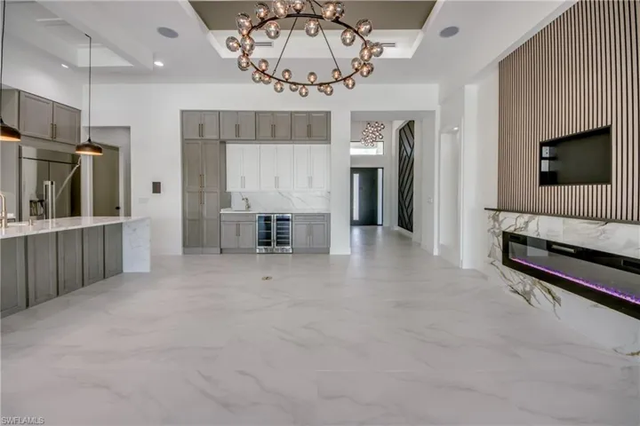 Unfurnished living room with beverage cooler, hanging lights, a tray ceiling, and a fireplace
