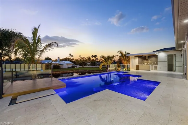 Pool at dusk featuring an outdoor kitchen and a patio