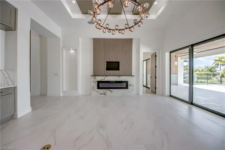 Living area with light marble finish flooring, a chandelier, a raised ceiling, and a fireplace