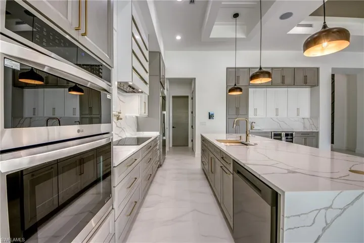 Kitchen featuring stainless steel appliances, light stone counters, dual tone cabinets, a large island, and decorative light fixtures