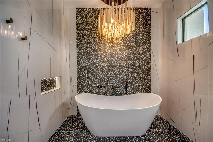 Bathroom with tile walls, a freestanding bath, tile patterned floors, and a chandelier
