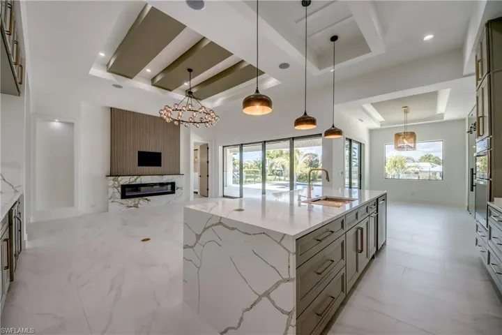 Kitchen featuring light stone counters, a large island with sink, suspended lighting, a high end fireplace, and open floor plan