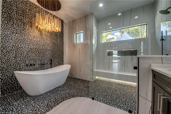 Bathroom featuring vanity, a soaking tub, tile walls, a marble finish shower, and recessed lighting