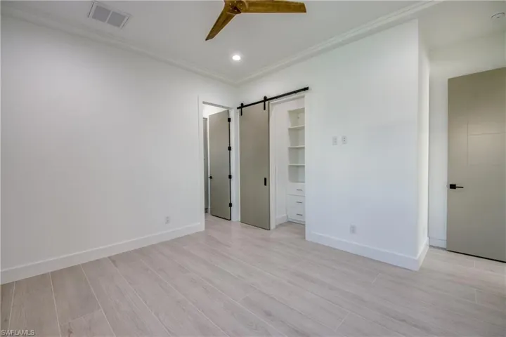 Unfurnished bedroom featuring a barn door, wood tiled floors, a ceiling fan, crown molding, and recessed lighting