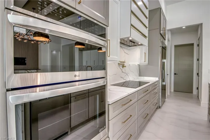 Kitchen featuring stainless steel appliances, light stone countertops, light marble finish floors, tasteful backsplash, and white cabinetry