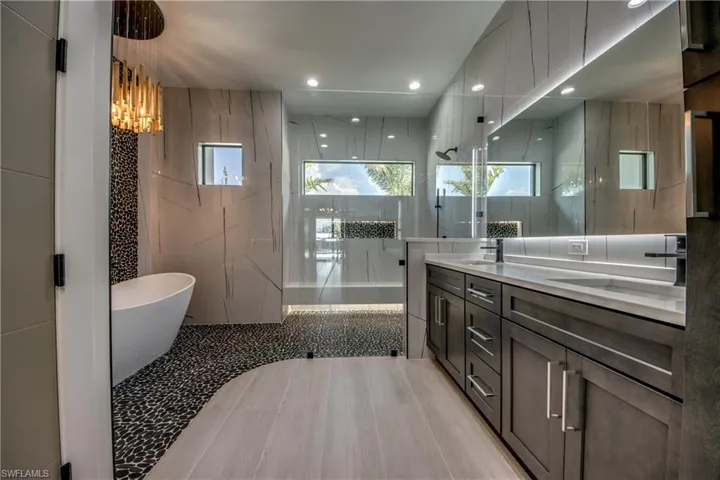 Bathroom with a freestanding bath, double vanity, tile walls, a marble finish shower, and recessed lighting