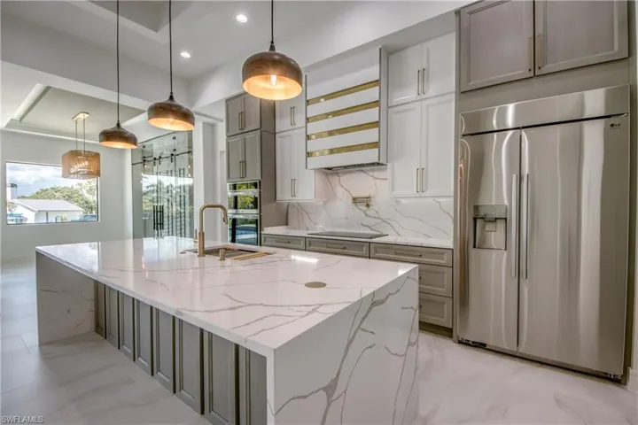 Kitchen featuring stainless steel appliances, light stone counters, and hanging light fixtures