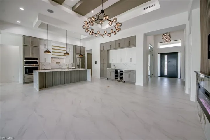 Kitchen featuring a chandelier, light marble finish floors, stainless steel appliances, backsplash, and beverage cooler
