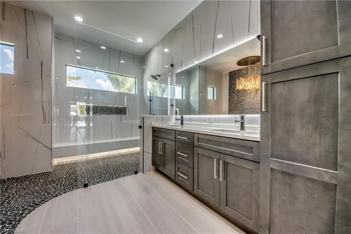 Bathroom with double vanity, a chandelier, and a combined bath / shower with marble appearance