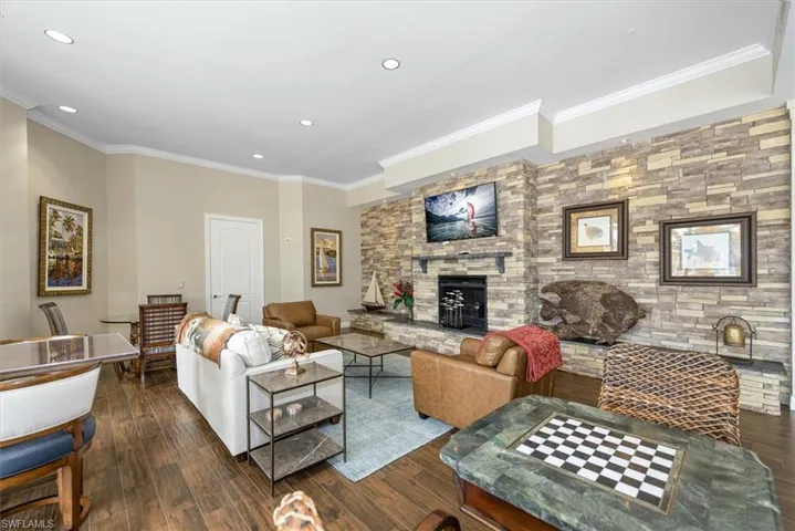 Living area with ornamental molding, dark wood-style flooring, recessed lighting, and a stone fireplace