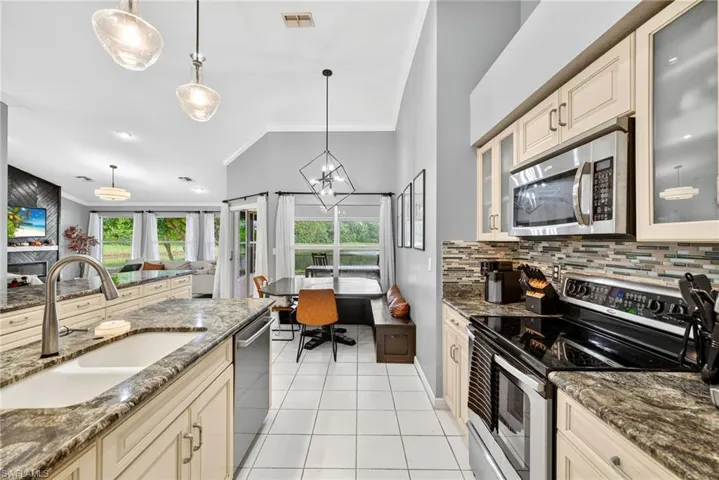 Kitchen with cream cabinets, decorative backsplash, dark stone counters, and crown molding