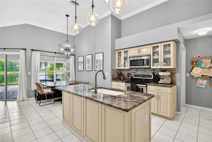 Kitchen with cream cabinetry, dark stone countertops, pendant lighting, stainless steel appliances, and a kitchen island with sink