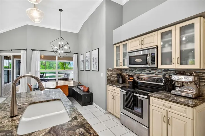 Kitchen featuring cream cabinetry, stainless steel appliances, hanging light fixtures, dark stone countertops, and crown molding