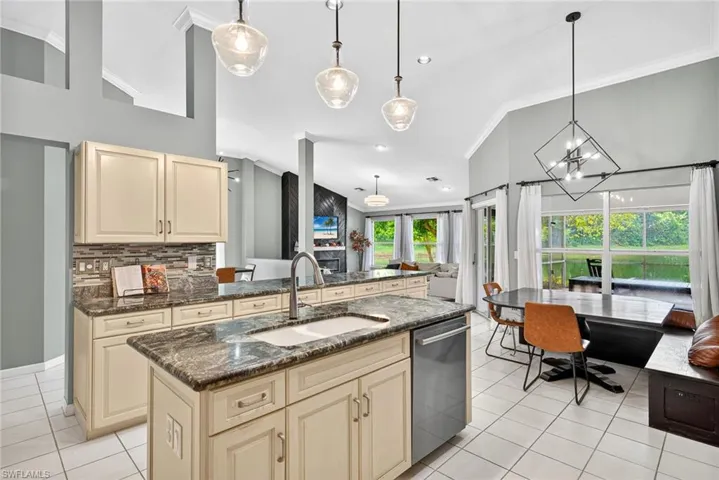 Kitchen featuring crown molding, dark stone counters, cream cabinetry, decorative light fixtures, and backsplash