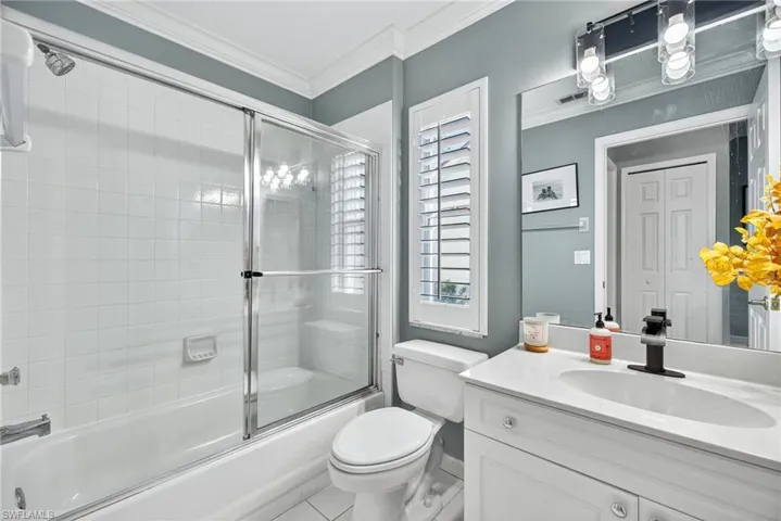Full bath with combined bath / shower with glass door, vanity, crown molding, and tile patterned floors