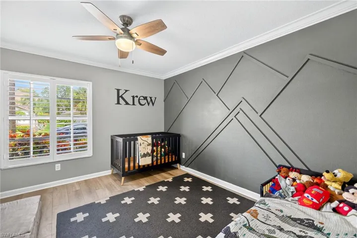 Bedroom with ornamental molding, a nursery area, light wood-style flooring, and a ceiling fan