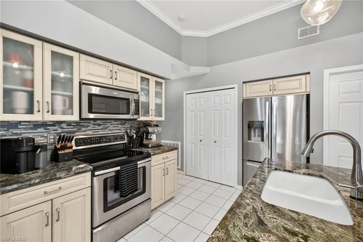 Kitchen with cream cabinets, stainless steel appliances, ornamental molding, dark stone countertops, and light tile patterned flooring