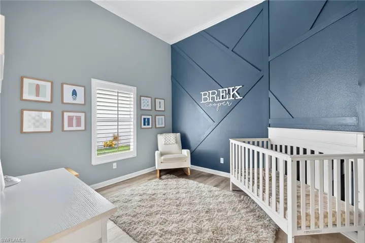 Bedroom with a crib, ornamental molding, and light wood-type flooring