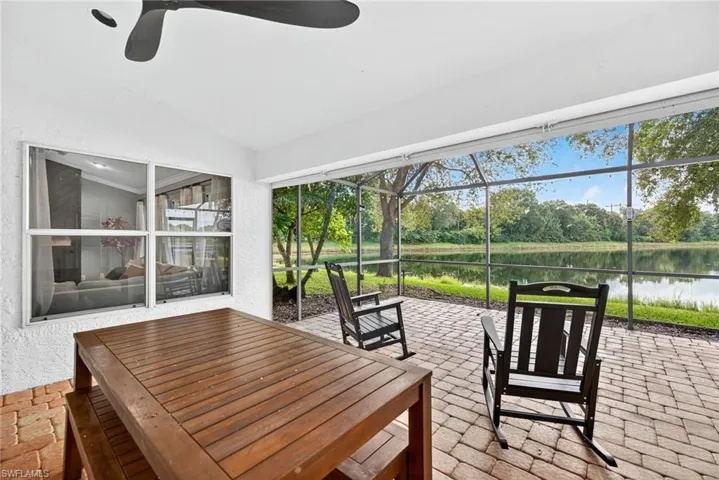 Sunroom with a patio area, a water view, a ceiling fan, and view of wooded area