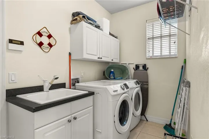 Clothes washing area featuring cabinets, light tile patterned floors, separate washer and dryer, and sink