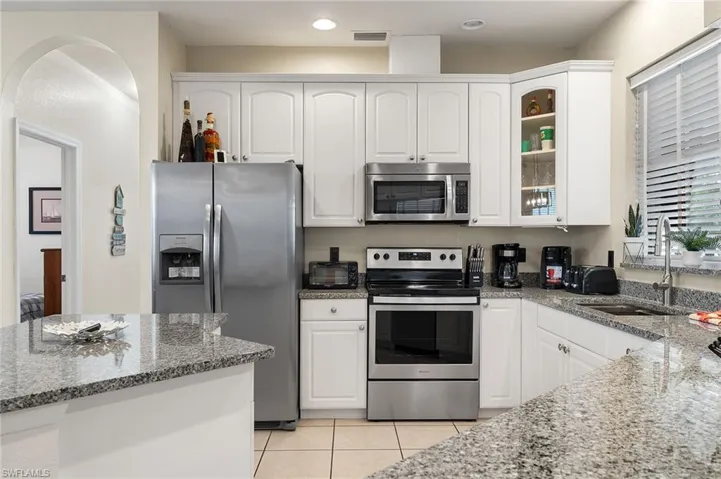 Kitchen featuring white cabinets, sink, light stone countertops, and stainless steel appliances