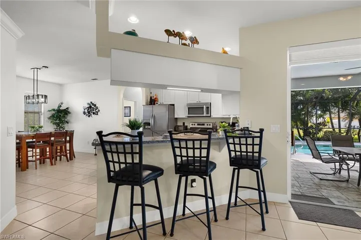Kitchen featuring kitchen peninsula, appliances with stainless steel finishes, light tile patterned floors, white cabinetry, and a breakfast bar area