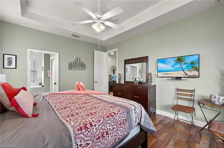 Bedroom featuring dark wood-type flooring, ensuite bathroom, a raised ceiling, crown molding, and ceiling fan