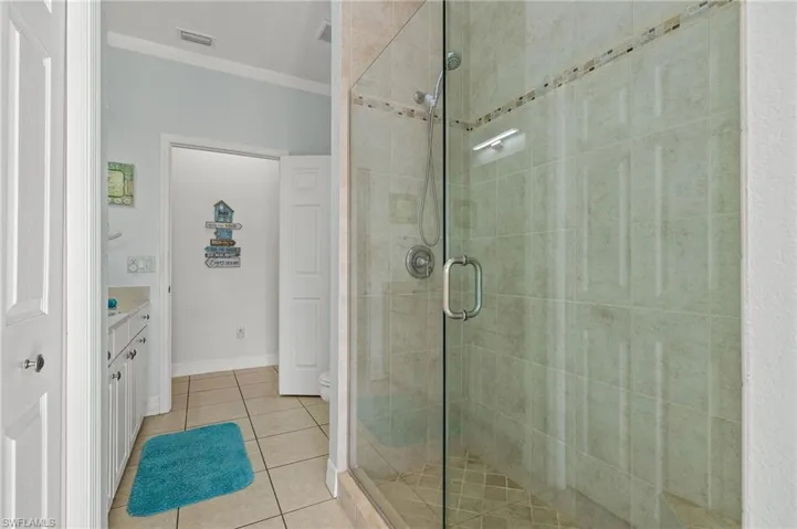 Bathroom with tile patterned floors, crown molding, an enclosed shower, toilet, and vanity