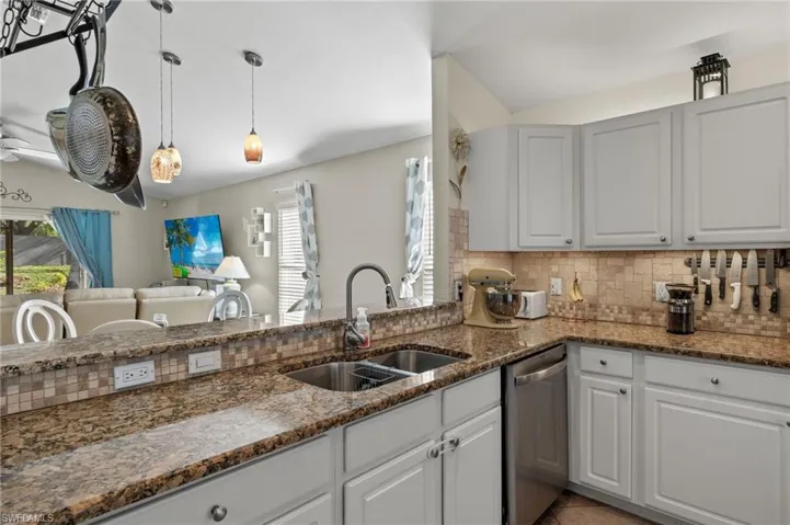 Kitchen featuring white cabinets, decorative backsplash, stainless steel dishwasher, and sink