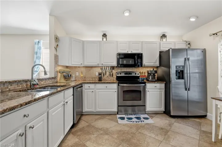 Kitchen featuring tasteful backsplash, stainless steel appliances, sink, dark stone countertops, and white cabinets