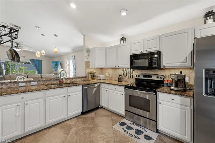 Kitchen with appliances with stainless steel finishes, sink, dark stone countertops, white cabinetry, and hanging light fixtures