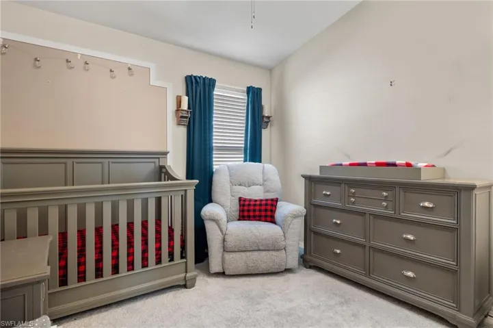 Bedroom featuring a crib, lofted ceiling, and light carpet