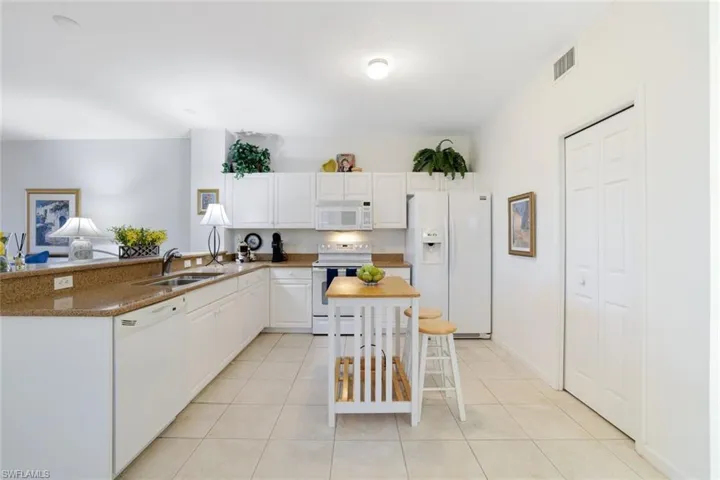 Kitchen with white appliances, white cabinets, light tile patterned flooring, and dark stone countertops