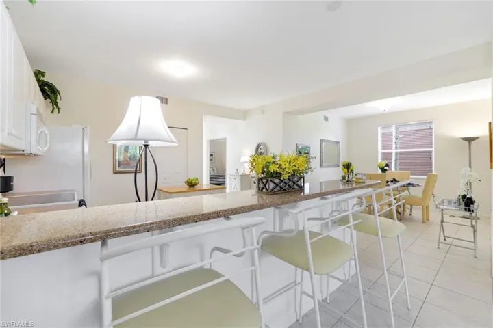 Kitchen featuring white cabinetry, light stone countertops, light tile patterned floors, a peninsula, and a kitchen bar