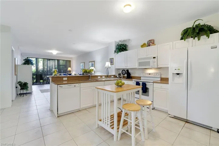 Kitchen featuring white appliances, white cabinetry, a peninsula, light tile patterned floors, and expansive windows