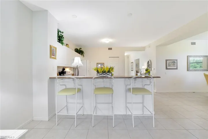Kitchen featuring a peninsula, white cabinetry, a kitchen bar, light tile patterned floors, and dark stone countertops