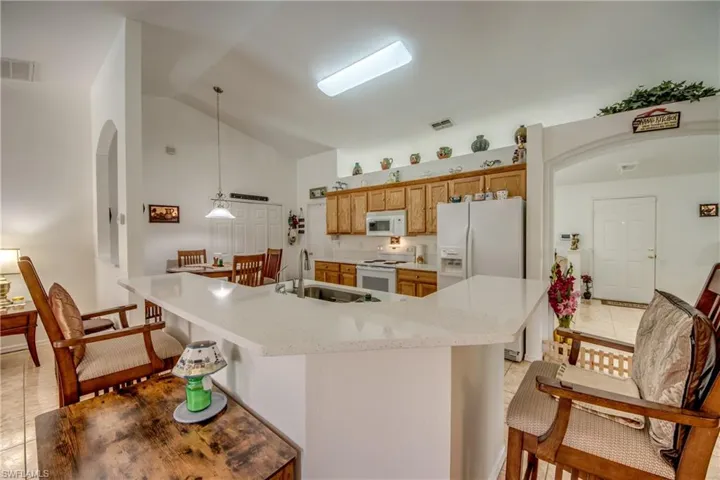 Kitchen featuring white appliances, vaulted ceiling, light tile patterned floors, pendant lighting, and a kitchen breakfast bar