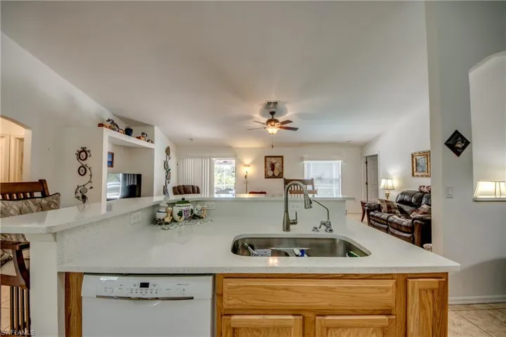 Kitchen with arched walkways, white dishwasher, open floor plan, and light stone counters