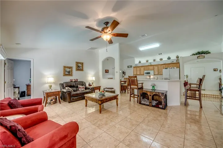 Living room featuring light tile patterned floors, arched walkways, ceiling fan, and vaulted ceiling