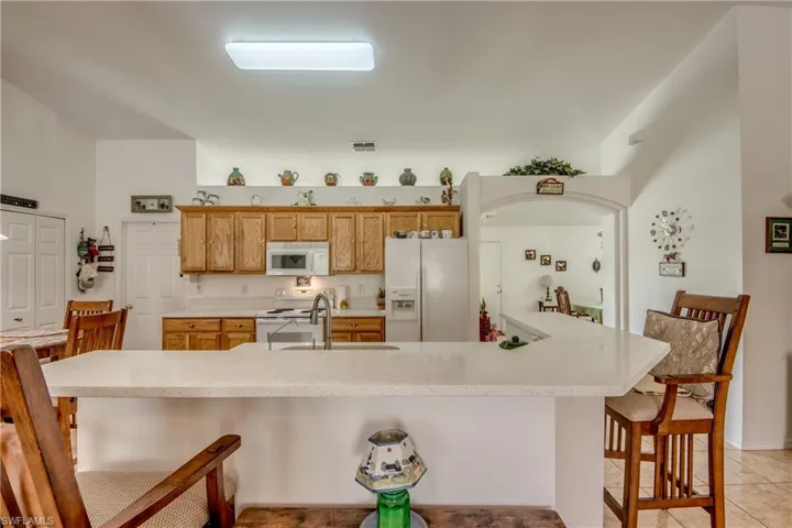 Kitchen with white appliances, a kitchen breakfast bar, a spacious island, light tile patterned floors, and light stone countertops