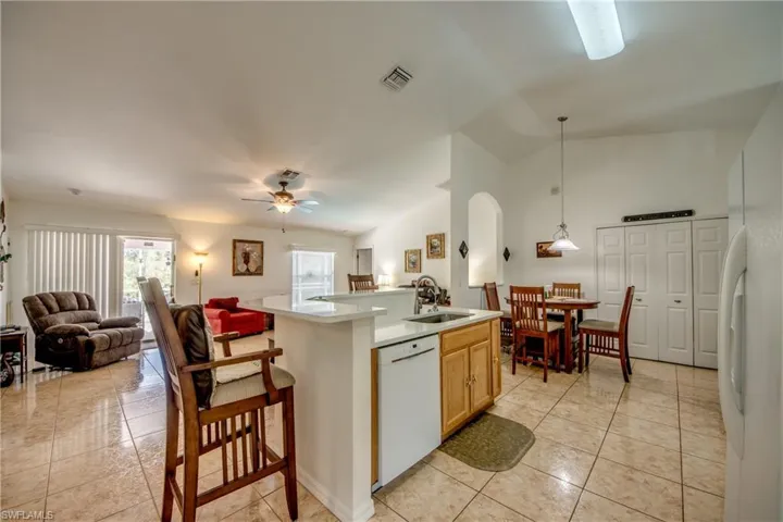 Kitchen featuring lofted ceiling, an island with sink, open floor plan, white appliances, and arched walkways