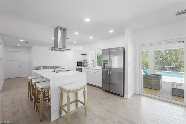 Kitchen with stainless steel appliances, island range hood, recessed lighting, white cabinets, and a breakfast bar area