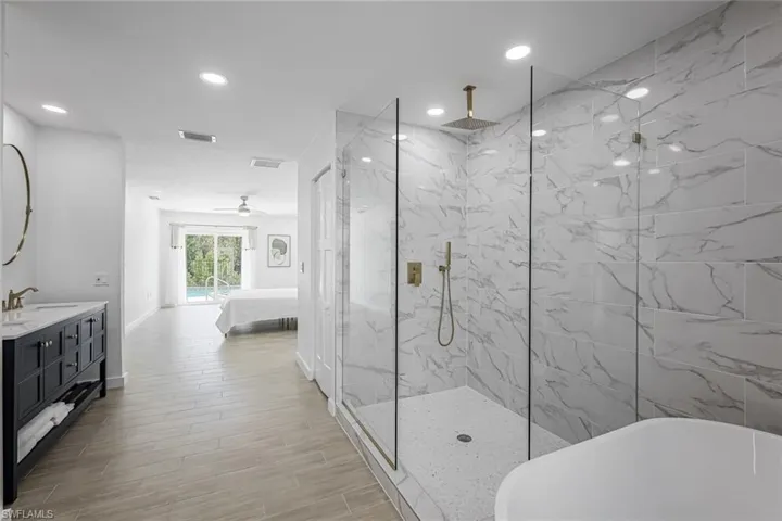 Ensuite bathroom with a freestanding tub, double vanity, a marble finish shower, wood finish floors, and recessed lighting