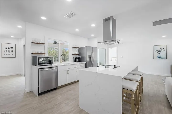 Kitchen with open shelves, white cabinetry, light stone counters, appliances with stainless steel finishes, and a kitchen breakfast bar