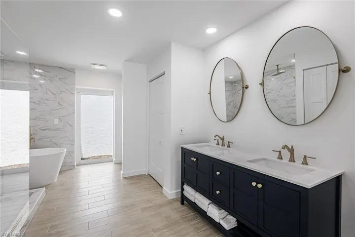 Bathroom featuring double vanity, wood tiled floors, a freestanding tub, recessed lighting, and a marble finish shower