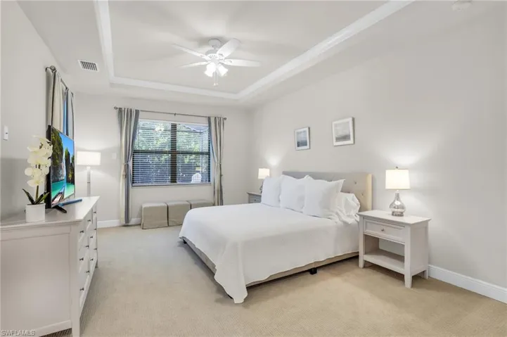 Bedroom featuring light carpet, ceiling fan, and a raised ceiling