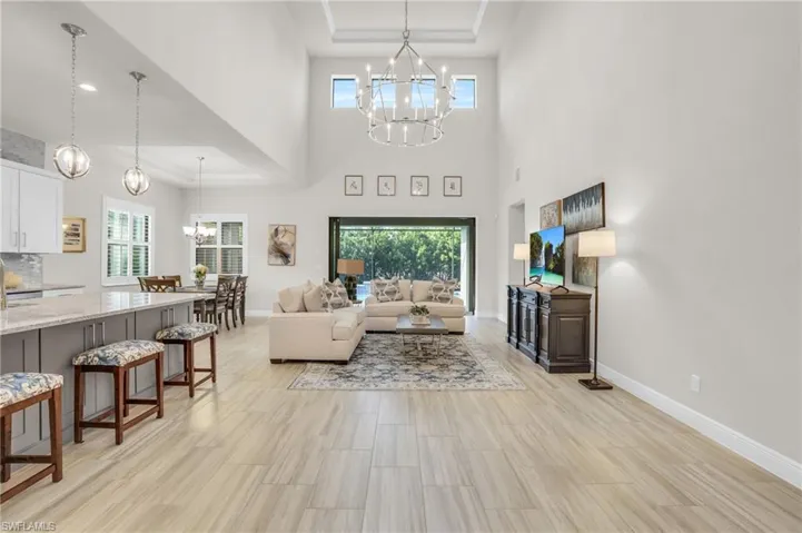 Living room featuring a tray ceiling, light tile flooring, a high ceiling, and a notable chandelier